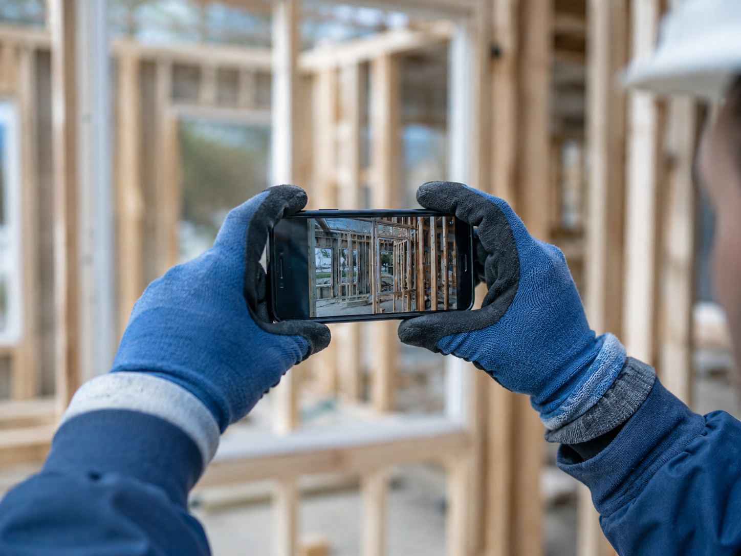 Field worker's gloved hands holding a phone, capturing a framing photo
